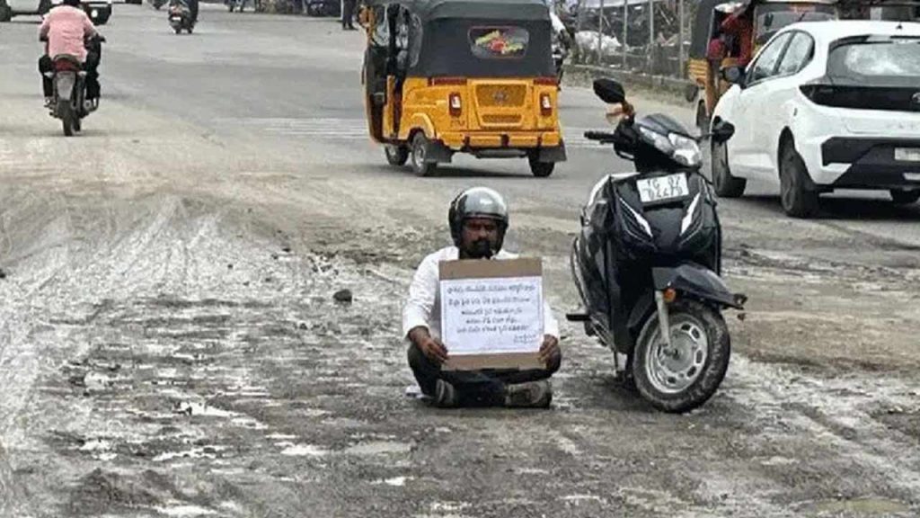 Social Worker Protests Potholes By Sitting On Damaged Road In Karimnagar